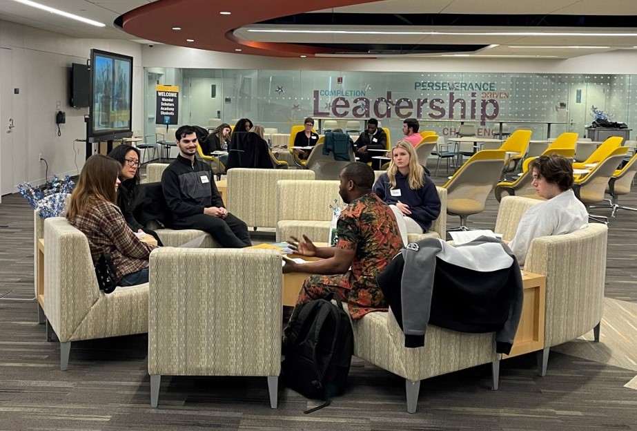 Group of students sitting around tables conversing and studying, under sign that says "Leadership."