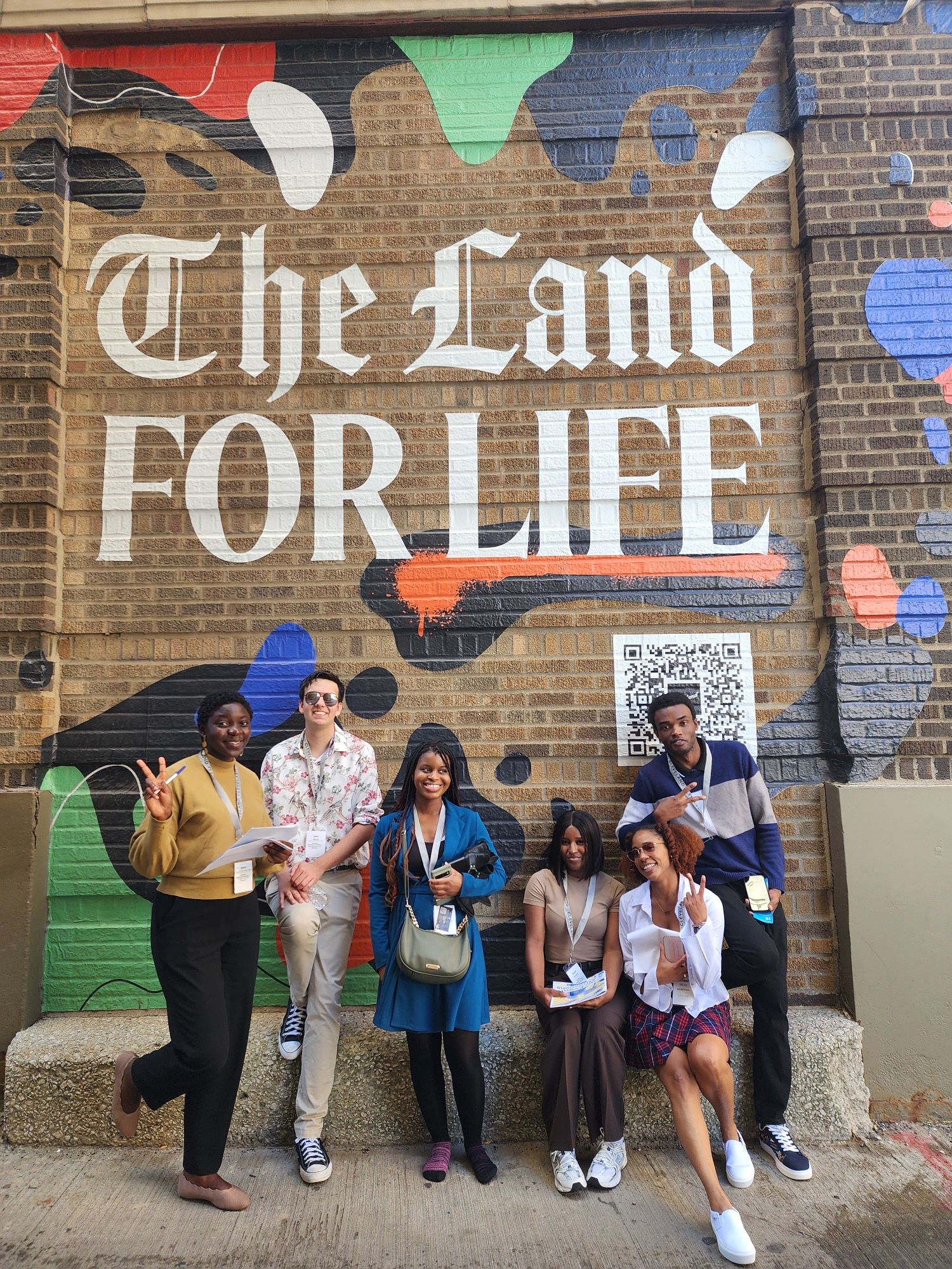Students posing under a mural that says "The Land for Life"
