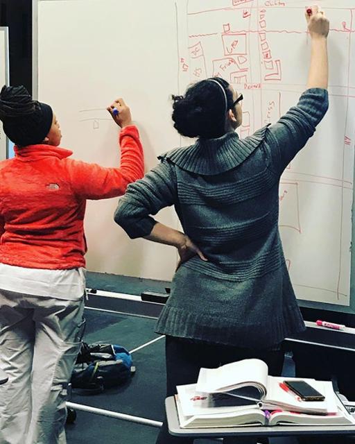Two female students writing on a dry-erase board