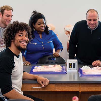 Male Student with other students and professor in classroom