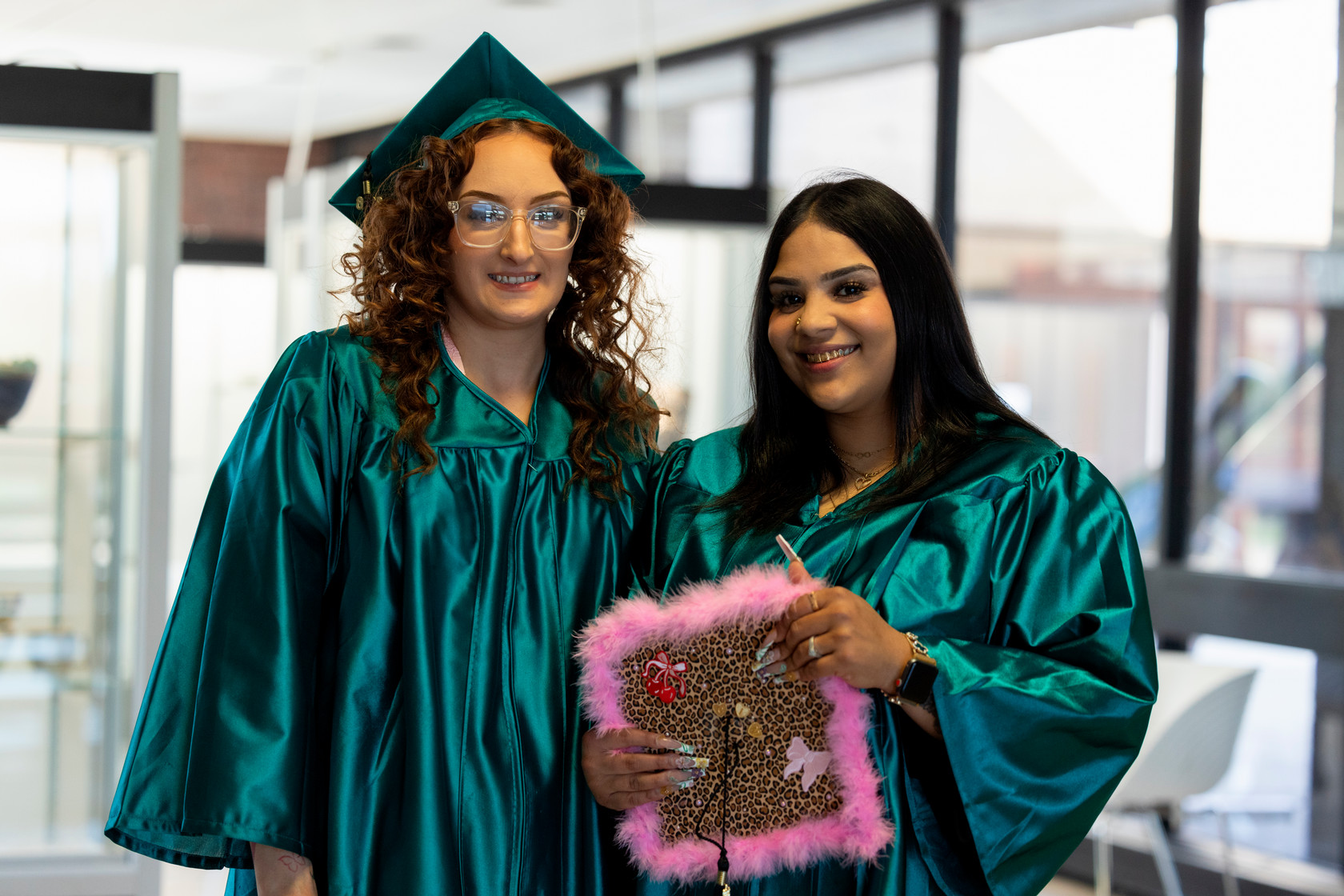 Two students stand side by side preparing for graduation showing decorated cap