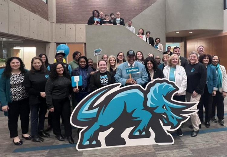 Tri-C President Dr. Baston grouped with team members behind big Triceratops prop
