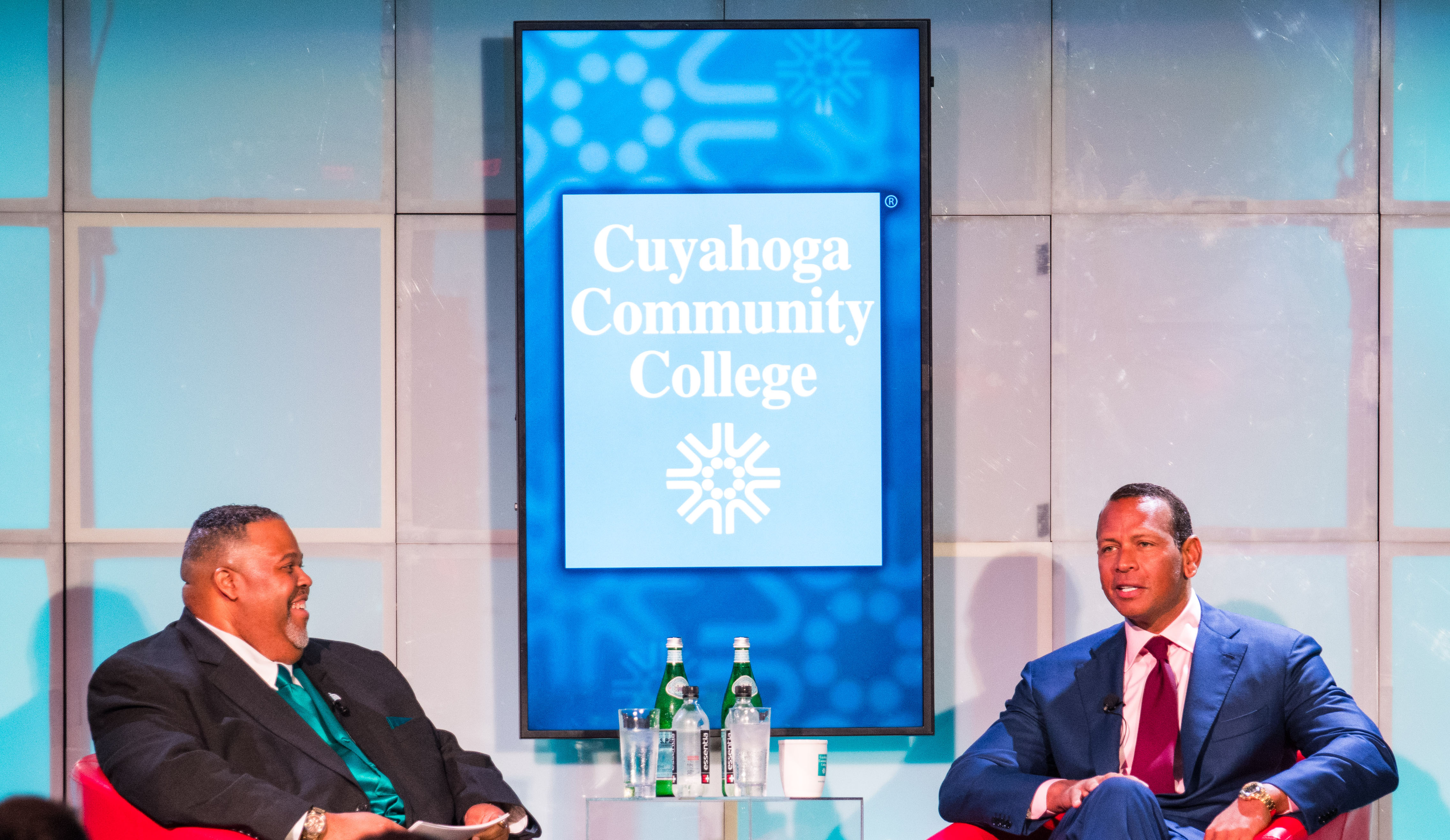 Tri-C President Dr. Michael Baston in conversation with Alex Rodriquez. Seated on stage in red club chairs under the Cuyahoga Community College logo and signage 