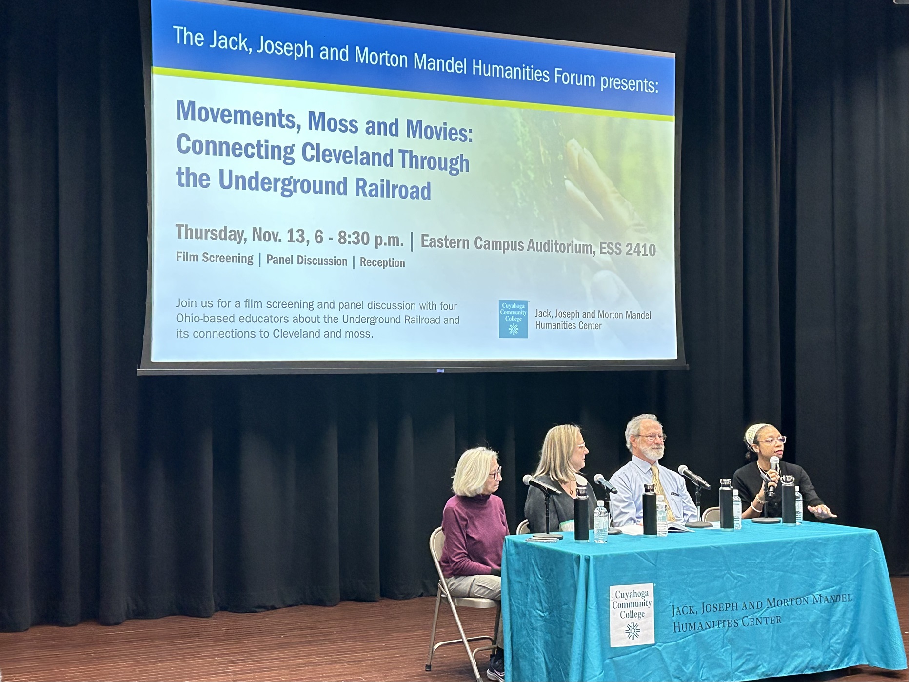 Four people sitting on a stage in front of a slide that reads, "Movements, Moss and Movies: Connecting Cleveland Through the Underground Railroad"