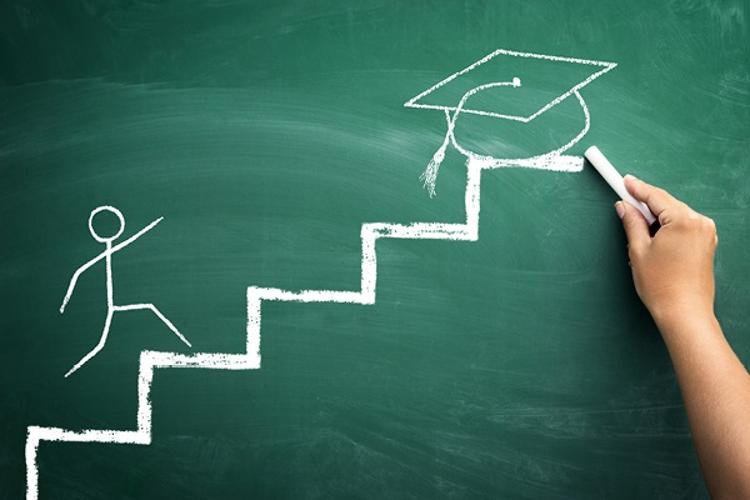 Chalkboard drawing of stick figure climbing steps toward graduation cap