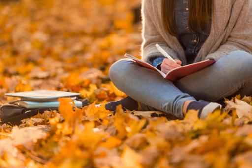 Photo of student sitting on leaf-filled lawn studying