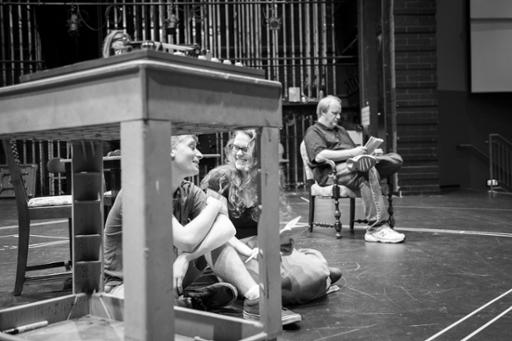 A photo from a rehearsal for A View from the Bridge. The picture shows two actors sitting next to a table and another in a distant chair