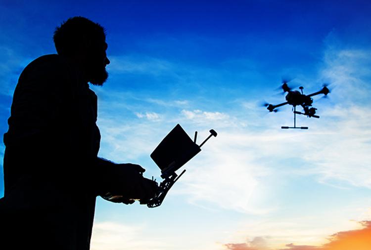 Silhouette of a man operating a drone against a twilight sky