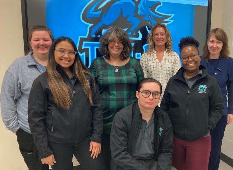 Group of six females and one male in front of Tri-C logo