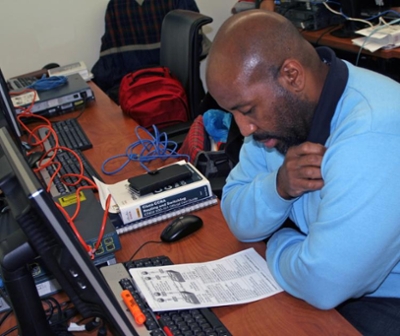 Man bent over a schematic in front of a computer board
