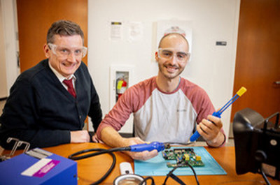 two students with their heads down working in robotics