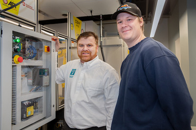 faculty and student looking at the camera and smiling; working on a CNC machine