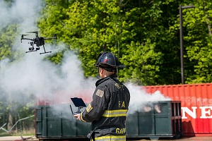 Firefighter in uniform flying drone with smoke in background